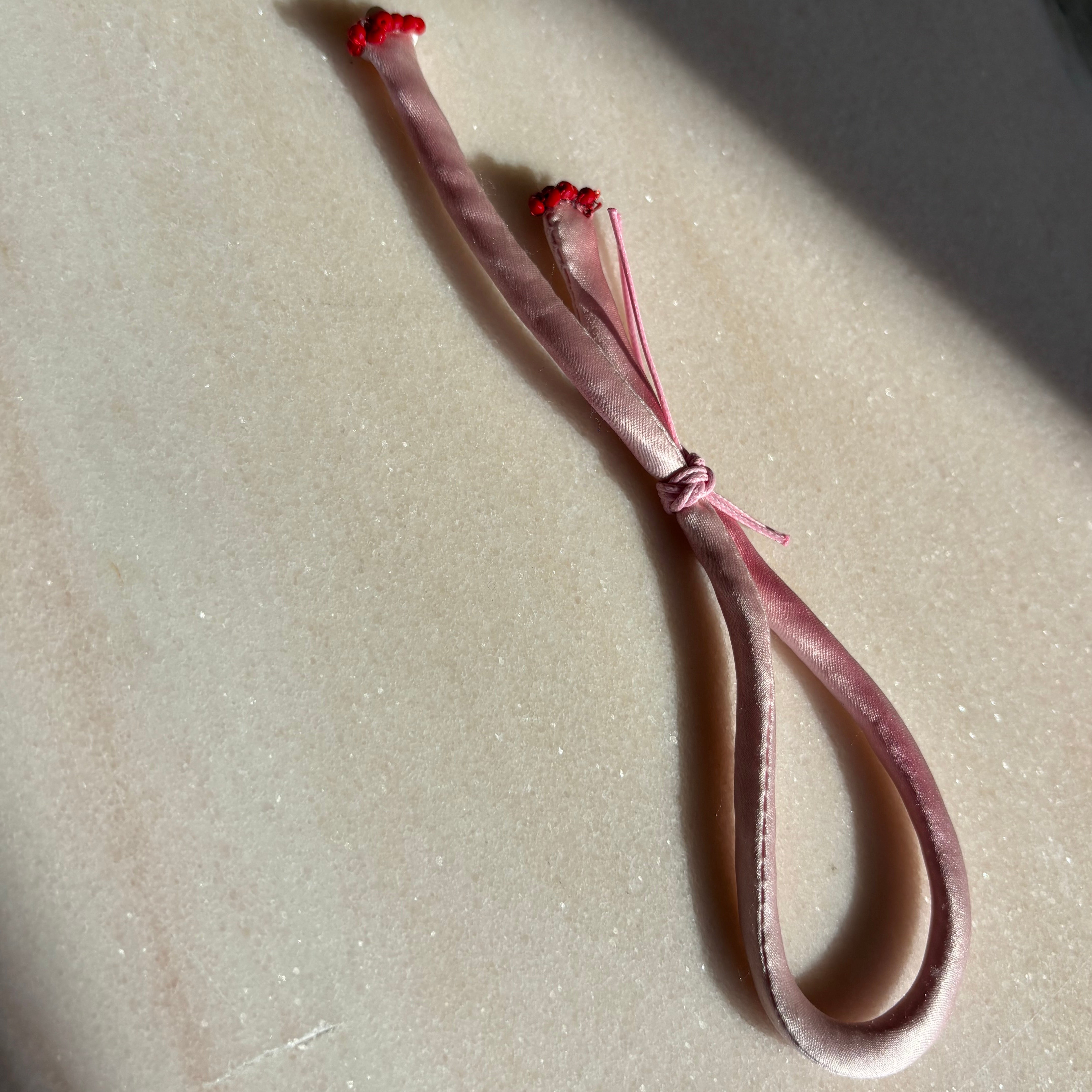 Pink silk adjustable bracelet finished with red spinel and mother of pearl clover and gold cord button slides up and down