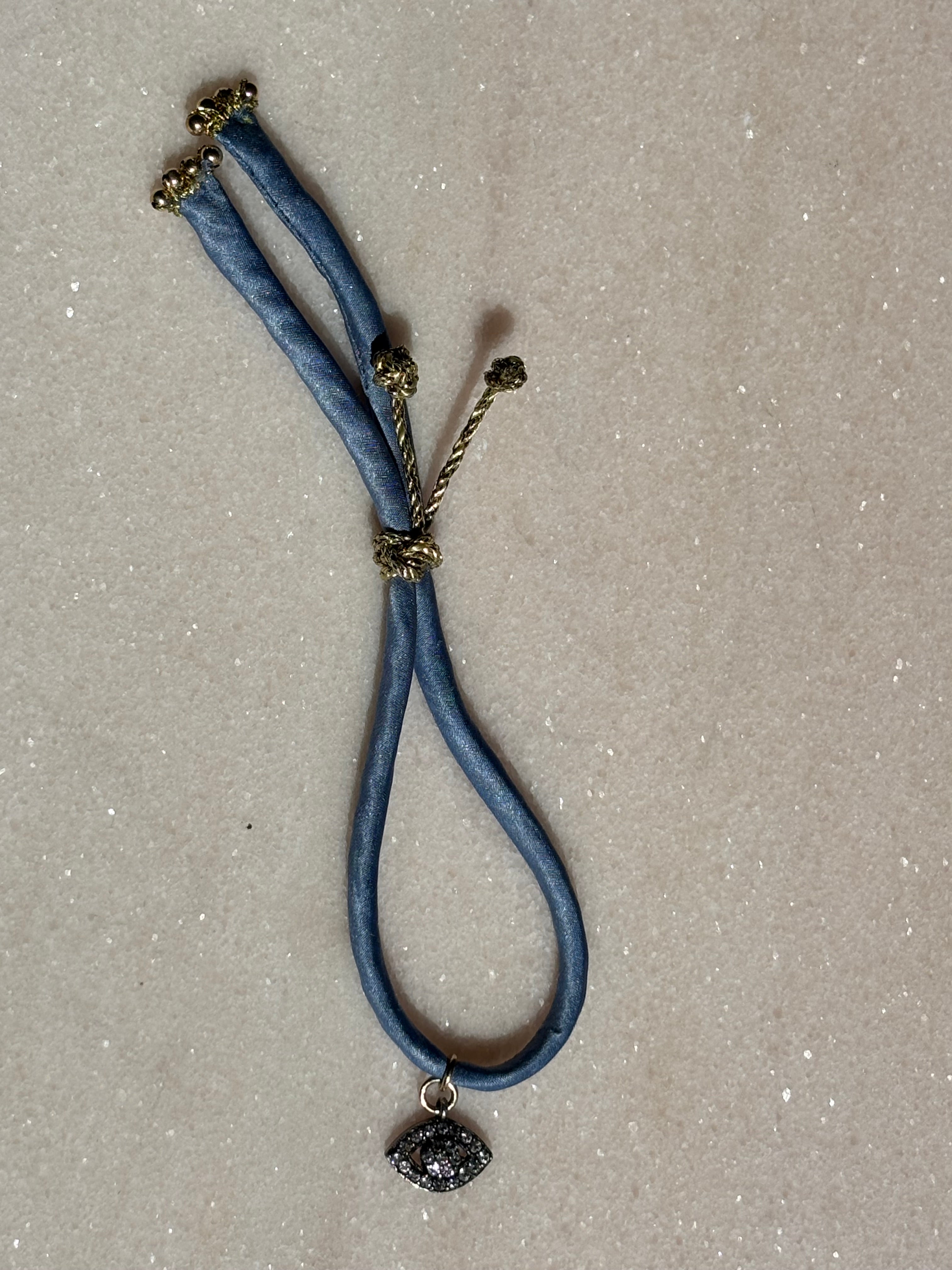 Side view of Blue Eyed Silk Kiss Bracelet showing blue jeans-colored silk cord and gold button by Boussidan.