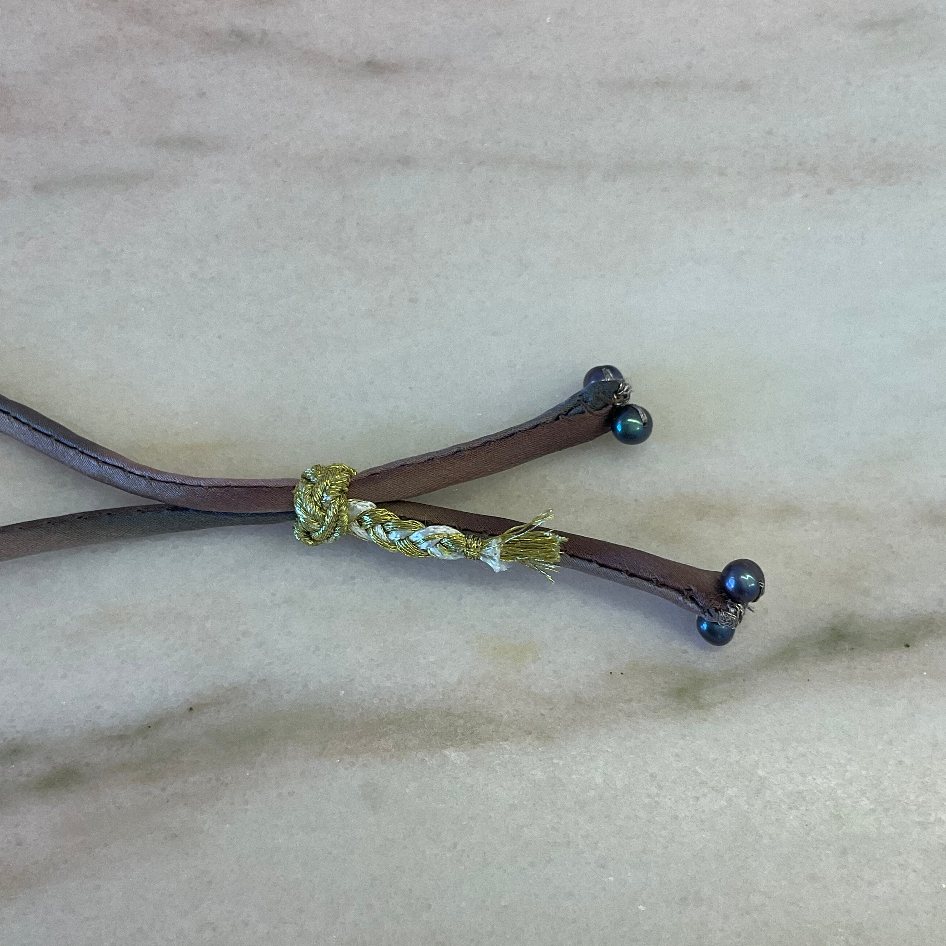 Close-up of black pearl ombre silk bracelet with adjustable gold button on silver silk