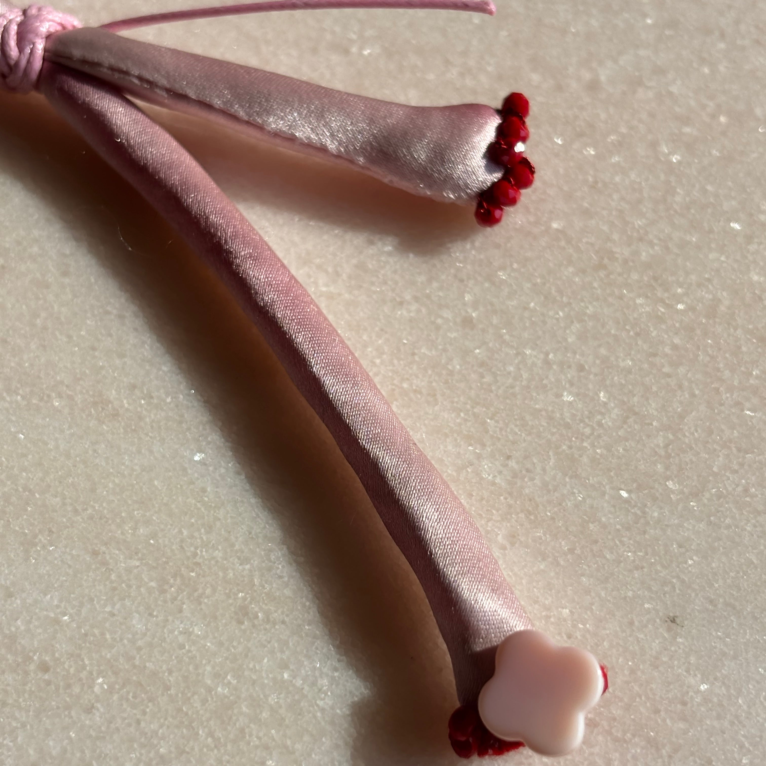 Pink silk adjustable bracelet finished with red spinel and mother of pearl clover and gold cord button slides up and down 