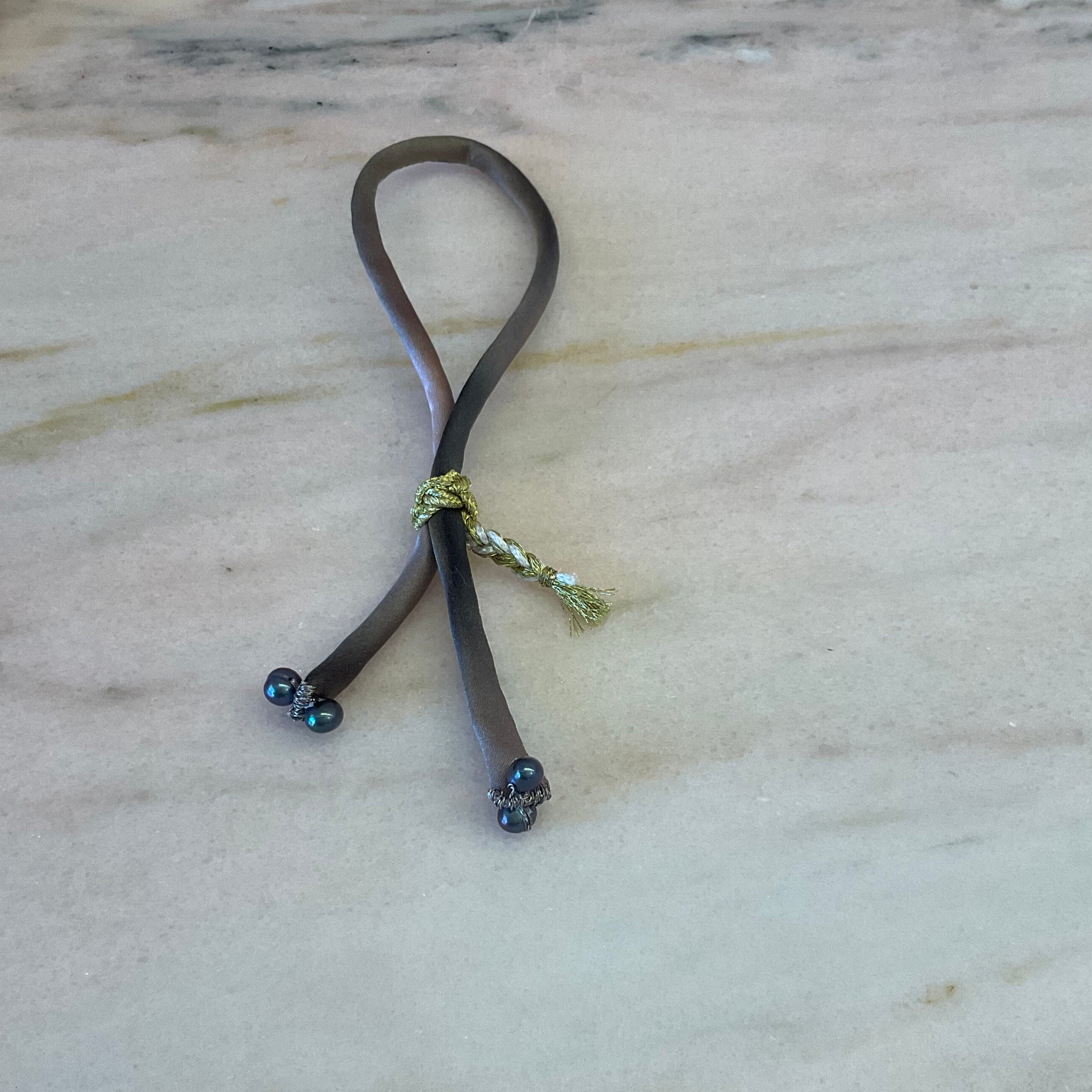 Ombre silk bracelet with black pearls, worn on wrist, showcasing gold braided button