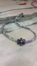 Load and play video in Gallery viewer, Floral patterned fabric cord  handmade amethyst flower gold filled center amethyst drops and a lavender sliding button adjustable to your wrist
