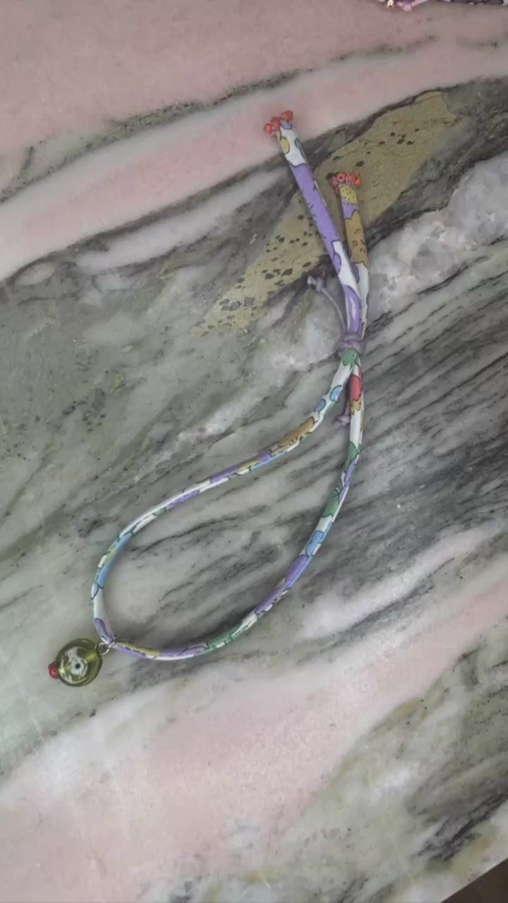 Video of Eye Envy Wild-Flowers Liberty Bracelet showing floral cord, eye glass charm, and adjustable purple button by Boussidan.