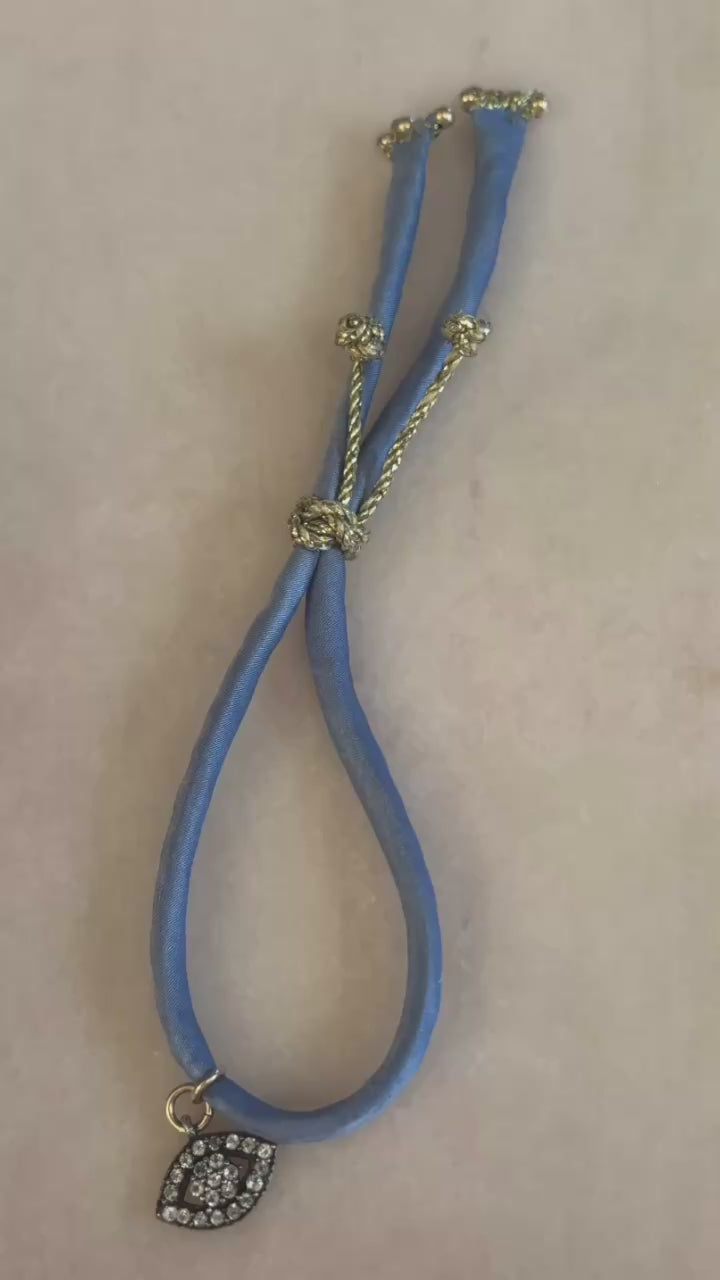Video of Blue Eyed Silk Kiss Bracelet showing blue jeans-colored silk cord, crystal flowered eye charm, and adjustable gold button by Boussidan.