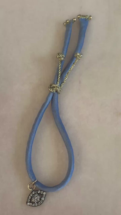 Video of Blue Eyed Silk Kiss Bracelet showing blue jeans-colored silk cord, crystal flowered eye charm, and adjustable gold button by Boussidan.