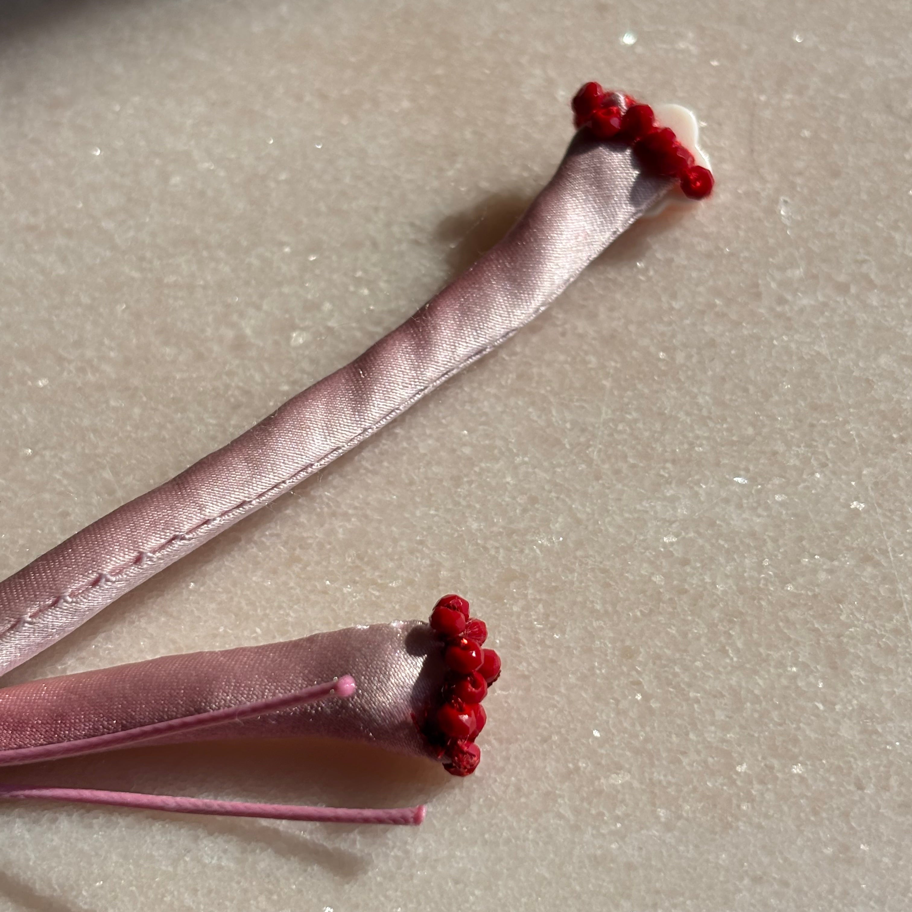 Pink silk adjustable bracelet finished with red spinel and mother of pearl clover and gold cord button slides up and down 
